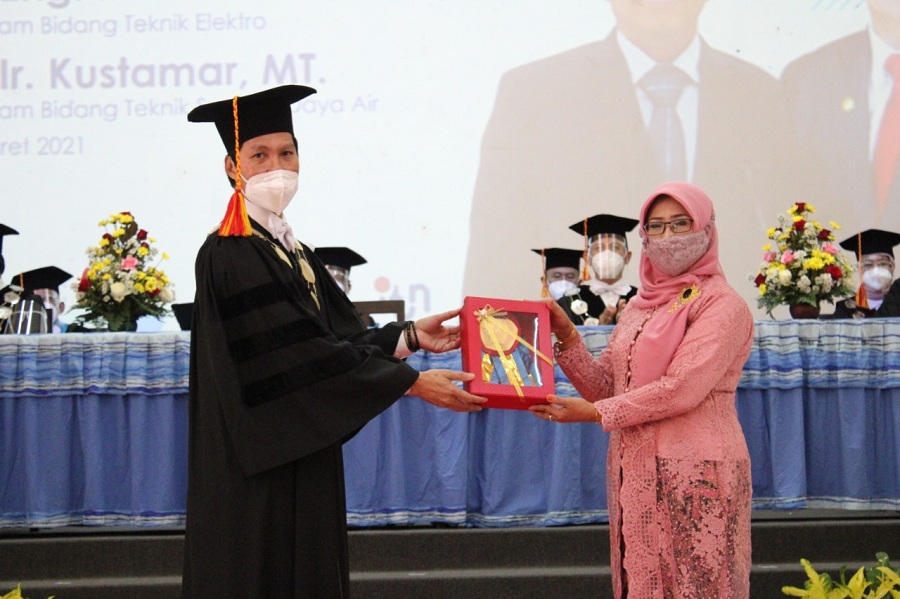 Ir. Ari Mukti, MT menerima gordon kehormatan dari Rektor ITN Malang Prof.Dr.Eng.Ir. Abraham Lomi, MSEE atas gelar guru besar yang diterima almarhum suaminya Prof.Dr.Ir. Kustamar, MT. (Foto: Yanuar/Humas)